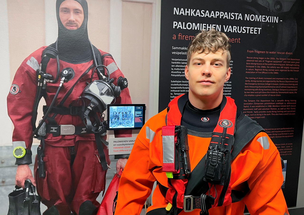 Kuvissa on mallina palomies Sam Zerlik. Hänen takanaan seinäjulisteessa on vesisukeltaja, palomies Antti-Pekka Paju. Paukkuliivin mittatilaustyönä tehtyihin taskuihin varusteet istuvat jämäkästi.