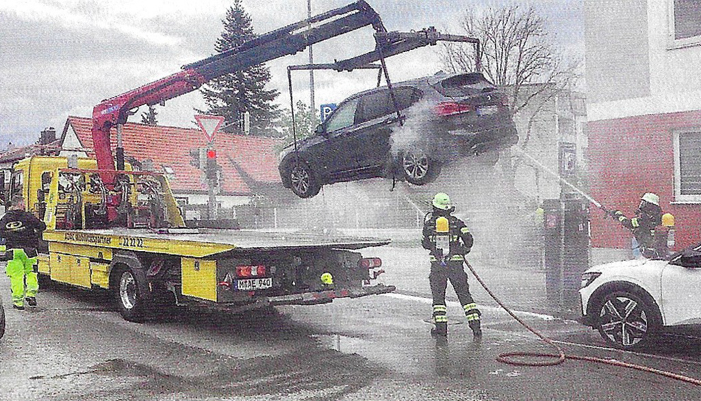 Sammuttajat valelevat sähköauton pohjaa kahdella suihkulla. Kuvakaappaus: Feuerwehr-Magazin 7/2025.